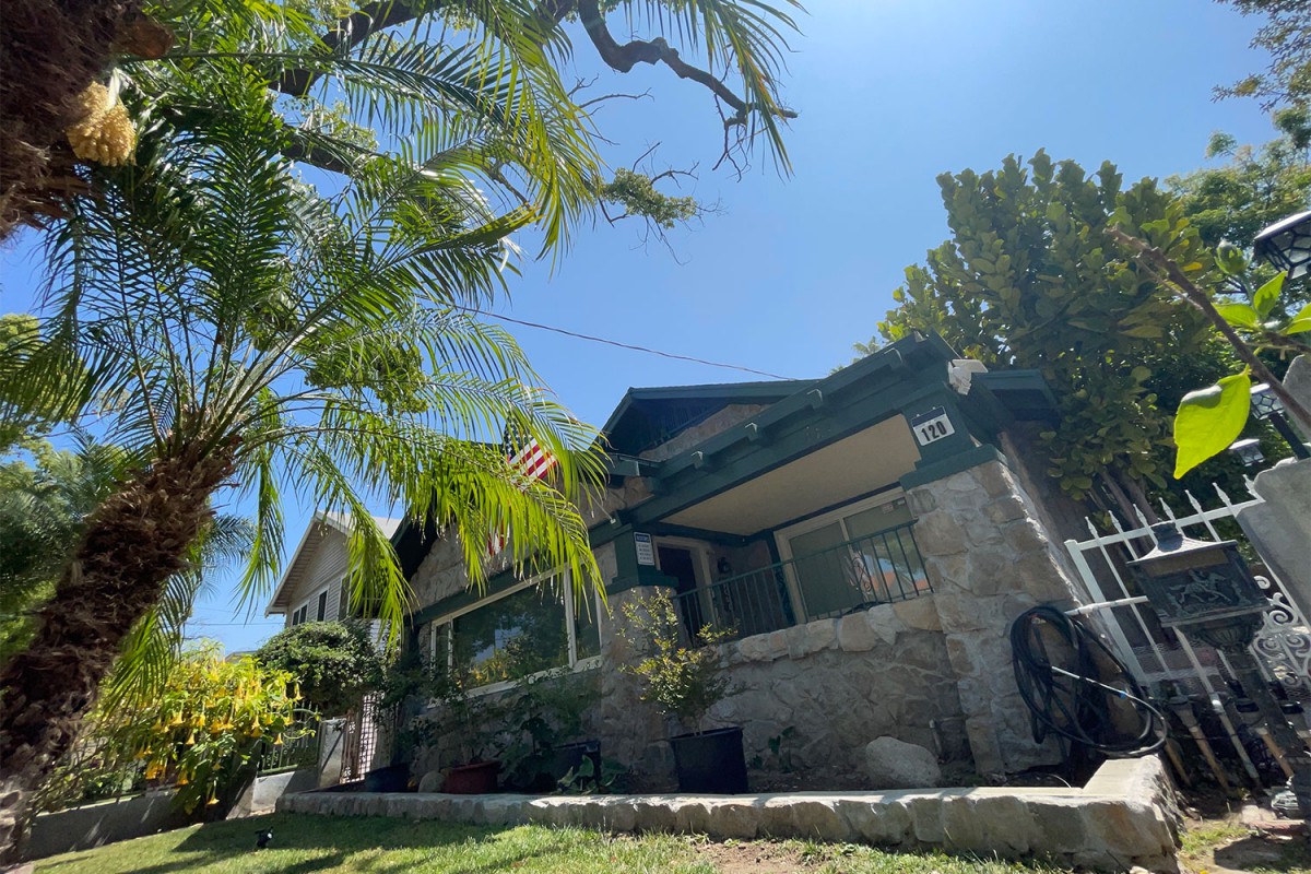 A charming bungalow with a stone facade, surrounded by palm trees on a sunny day.