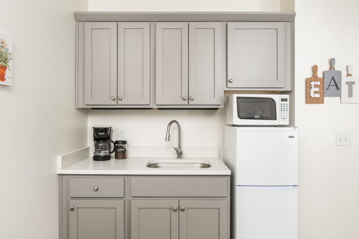 A compact kitchen area featuring grey cabinets, a sink, a microwave, and a refrigerator.