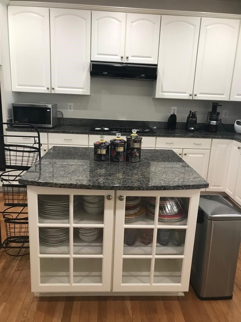 A modern kitchen with a central island, surrounded by white cabinets and various appliances.