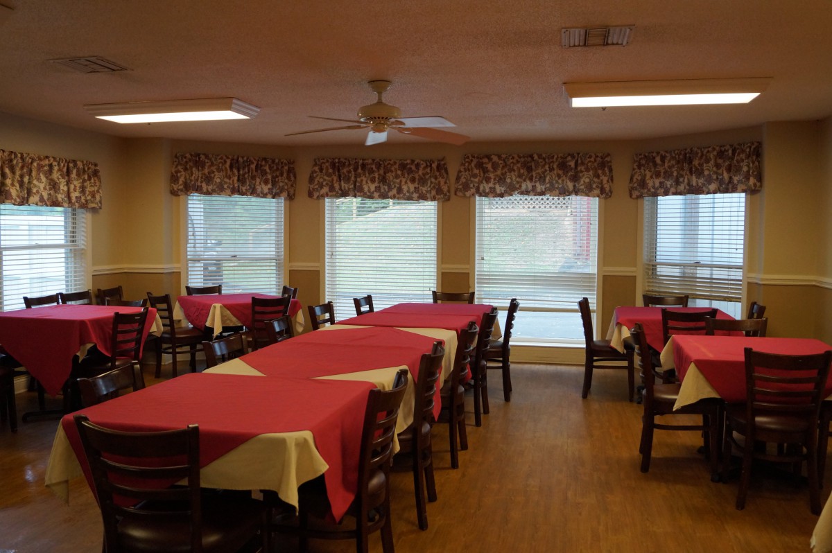 A dining room with tables covered in red tablecloths and chairs arranged around them.