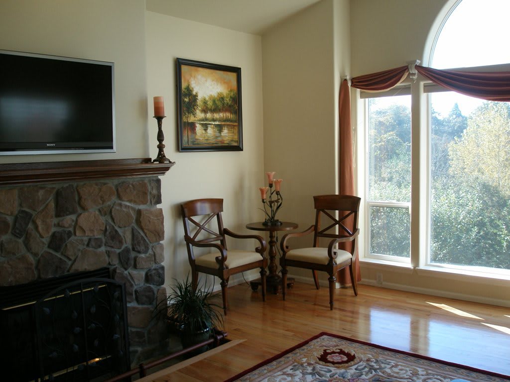 Cozy living room corner with a stone fireplace, elegant chairs, and a large window letting in natural light.