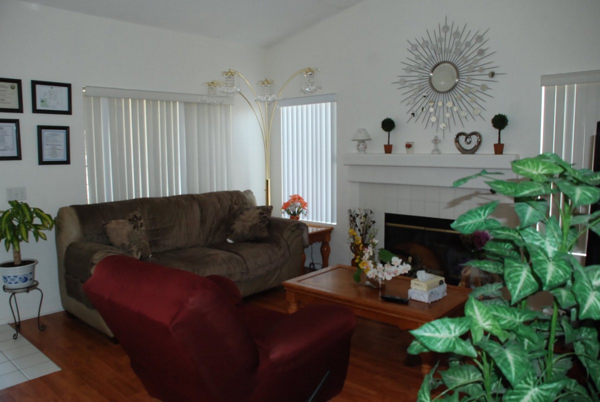 A cozy living room featuring a sofa, armchair, coffee table, and a decorated fireplace with window blinds.