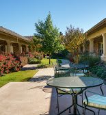 A serene outdoor patio area with tables and chairs surrounded by lush gardens and pathways.
