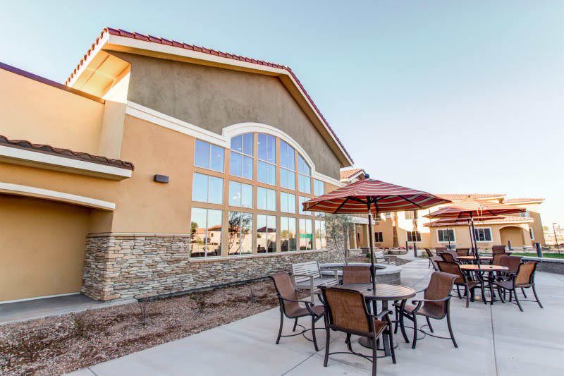 A modern building with a stone facade featuring outdoor seating with tables, chairs, and umbrellas.