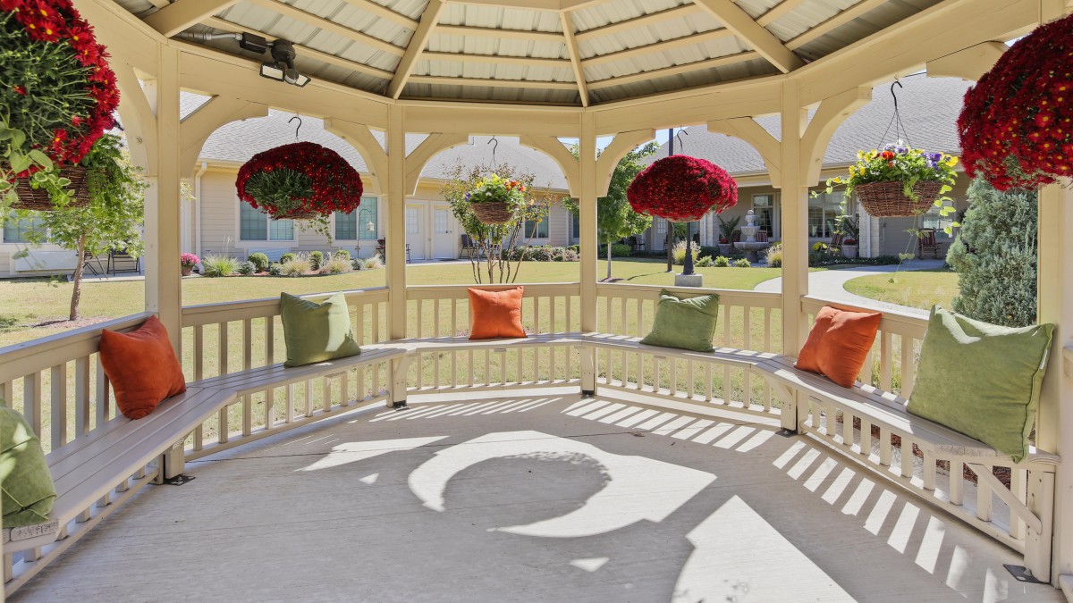 A cozy gazebo with colorful cushions and hanging flower baskets, casting intricate shadows on the concrete floor.