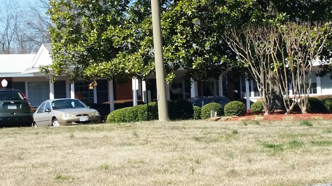 A suburban building surrounded by trees and bushes, with parked cars in the driveway.