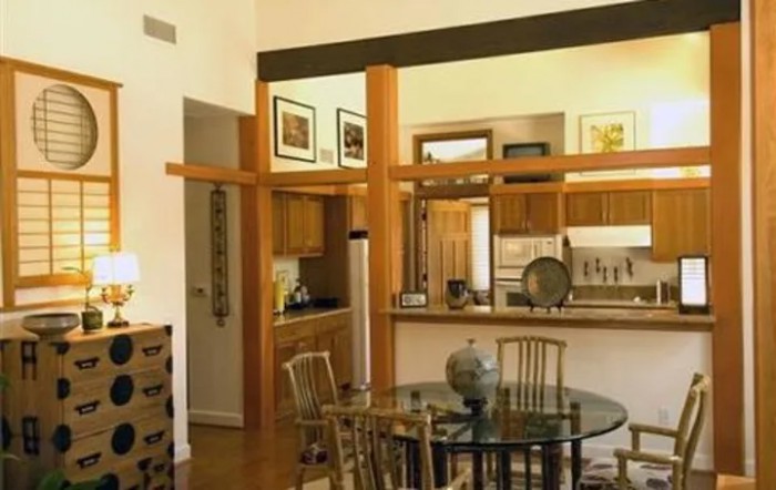 A cozy dining area with a glass table and wooden chairs, adjacent to an open kitchen featuring warm wooden accents and modern decor.