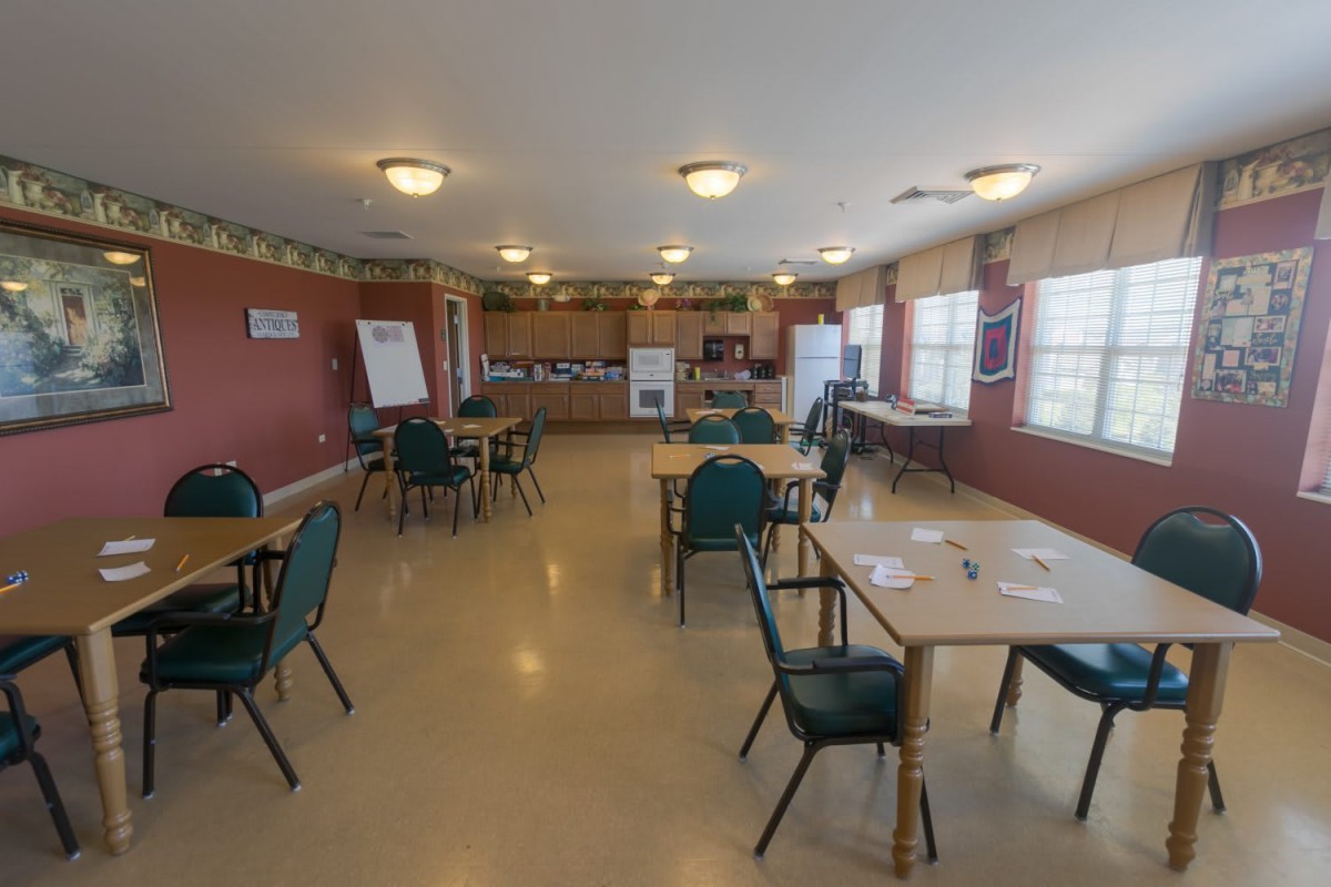 A communal dining area with tables and chairs, featuring a kitchen at the back.