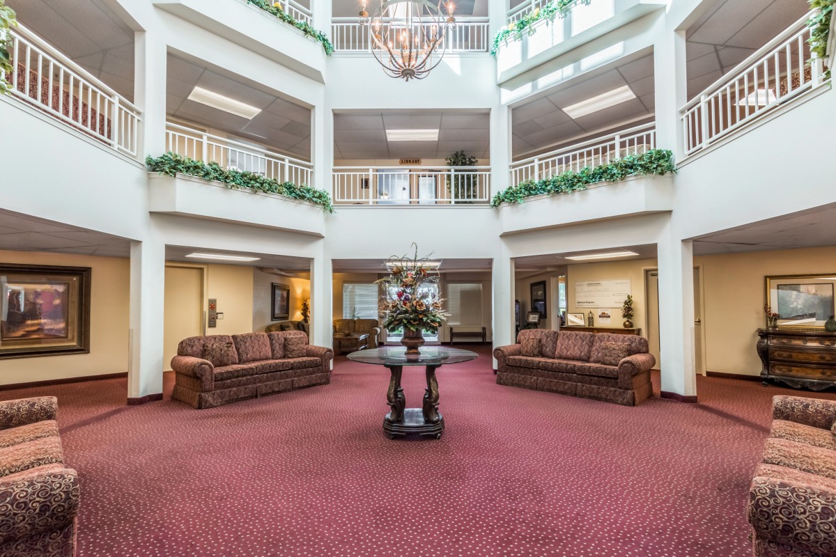 A spacious and elegant atrium lobby featuring sofas, a central table, plants, and a chandelier.