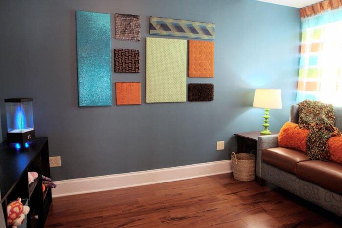 A contemporary living room features colorful abstract art panels adorning a blue wall, complemented by a cozy corner with a lamp.
