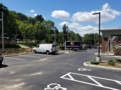 A view of a parking lot with several vehicles and greenery under a blue sky.