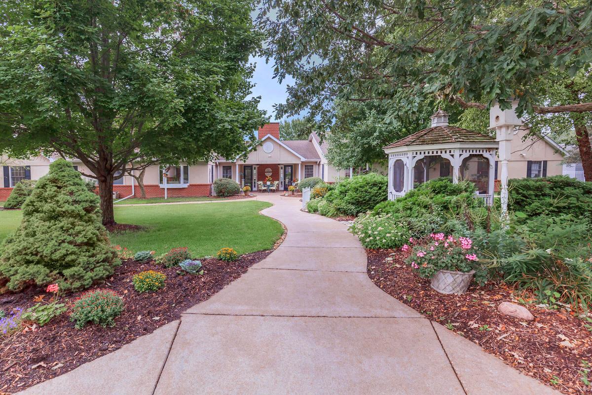 A scenic pathway leading to a house, surrounded by lush gardens and a charming gazebo.