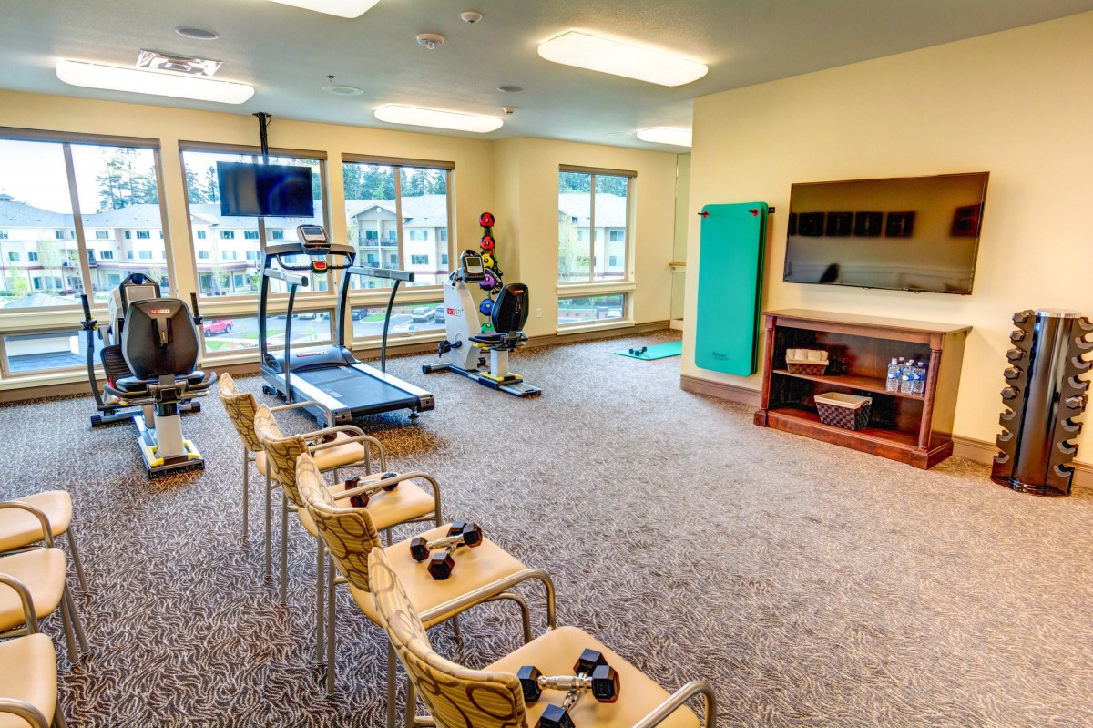 A well-lit fitness room equipped with treadmills, exercise bikes, and dumbbells.