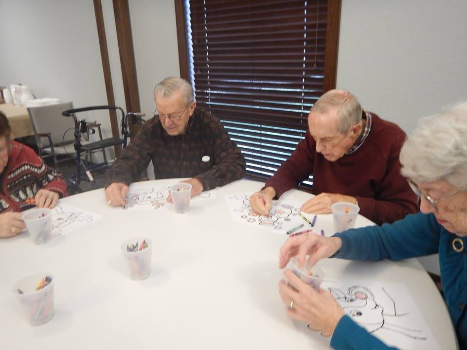 Elderly individuals engaged in a group craft activity at a table.