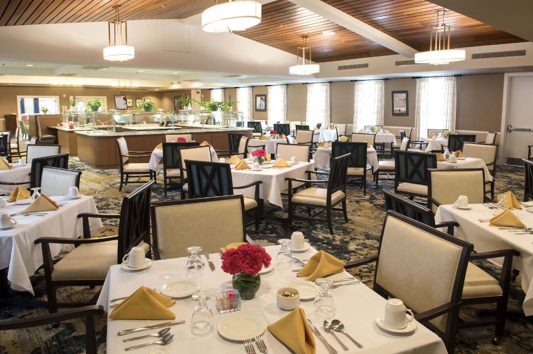 An elegantly set dining room with neatly arranged tables and chairs, featuring decorative flowers and fine tableware.