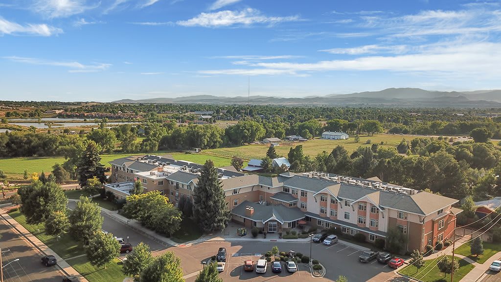 An aerial view of a countryside landscape with buildings surrounded by trees and greenery under a clear blue sky.