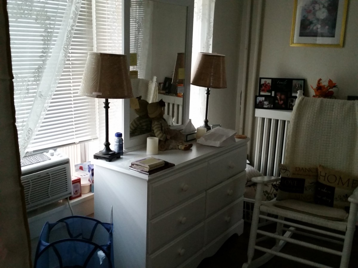 A cozy bedroom with a white dresser and two lamps in front of a window with blinds.