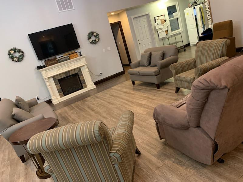 A cozy living room with multiple chairs, a sofa, a television mounted above a fireplace, and a hardwood floor.