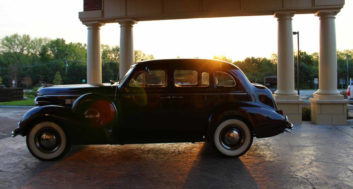 A classic vintage car is parked outdoors, basking in the warm glow of a sunset.