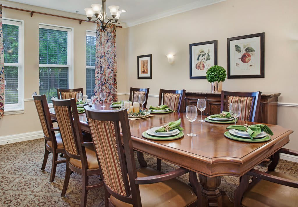 An elegant dining room with a set table, adorned with decorative place settings and illuminated by a chandelier.