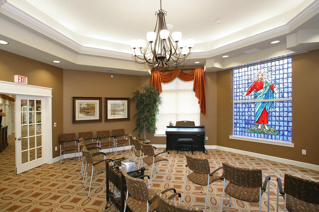A well-decorated meeting room featuring a chandelier, stained glass window, and office furniture.