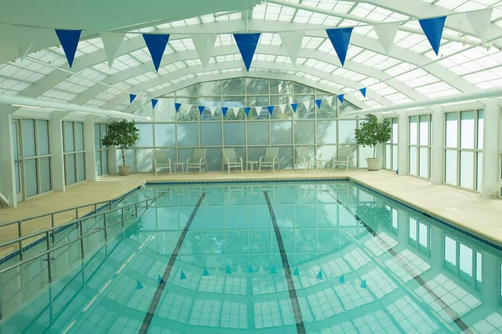 An indoor swimming pool with lanes and blue banners under a glass ceiling, allowing natural light to illuminate the space.