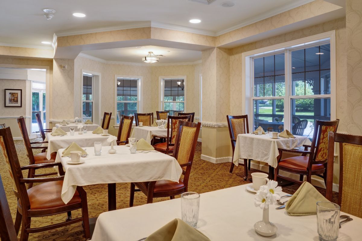 A well-lit dining area with neatly arranged tables and chairs, featuring large windows and elegant decor.
