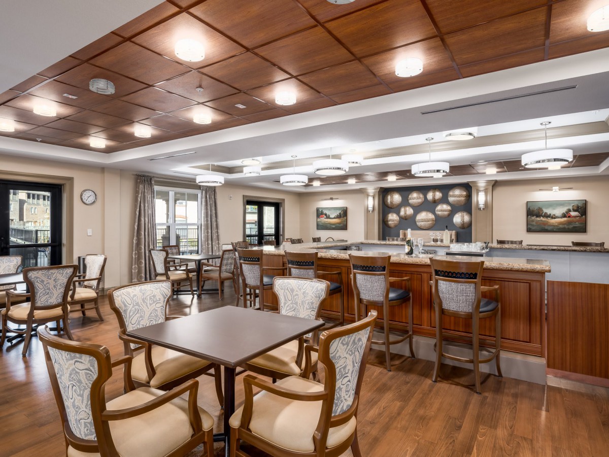 A cozy restaurant interior with a bar and seating area featuring wooden furniture and ceiling lights.