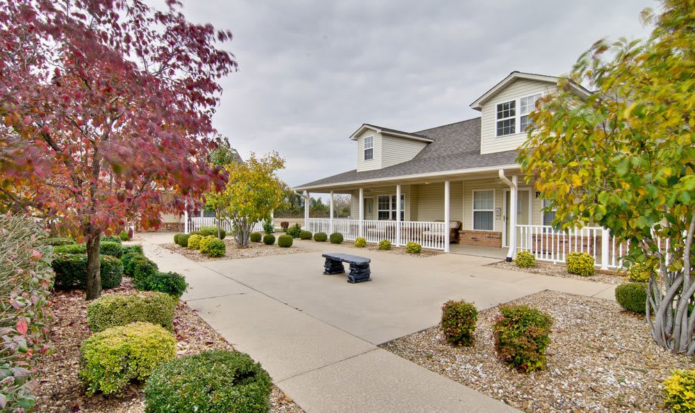 A charming house with a landscaped front yard, featuring a pathway and a bench surrounded by autumn foliage.