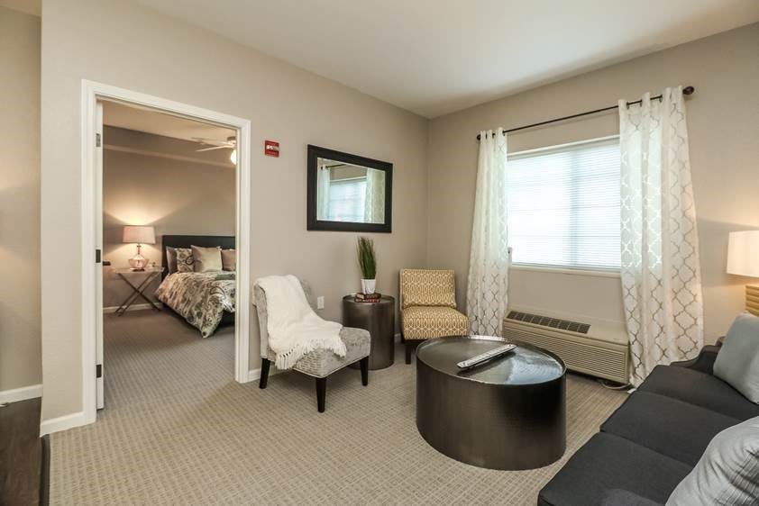 A modern living room with comfortable seating, a view into the bedroom, and elegant decor.