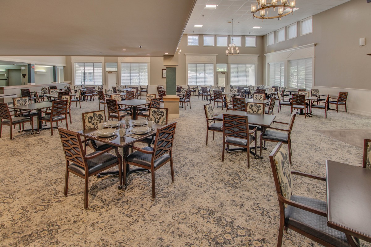 Spacious dining room with neatly arranged tables and chairs, featuring large windows and a chandelier.