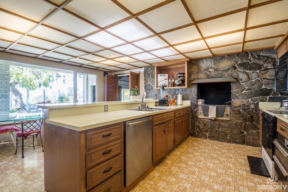 A retro-style kitchen featuring wood cabinets and a stone fireplace, with an island counter and overhead lighting.