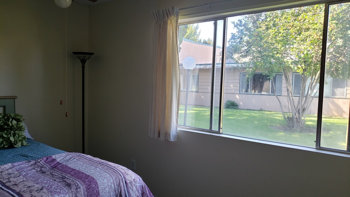 A bedroom with a bed and lamp, featuring a window with a view of the outdoors.