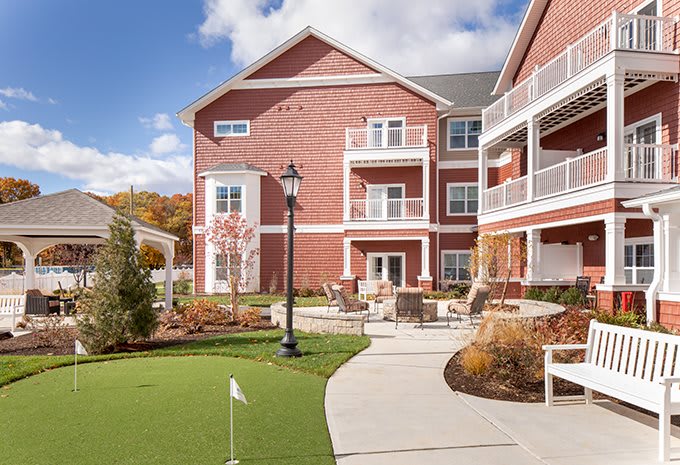 A sunny day at a residential building with brick exterior and well-maintained landscaping, featuring balconies and a walking path.