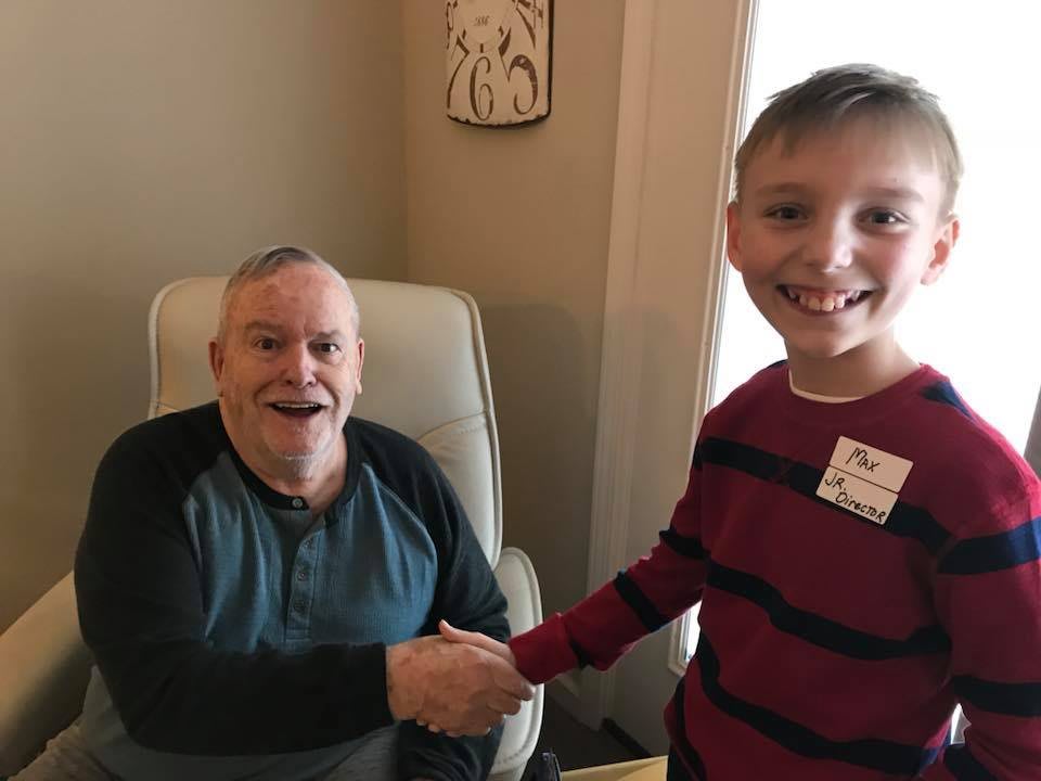 A young boy and an older man smiling and shaking hands indoors.