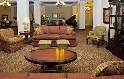 A hotel lobby featuring a comfortable seating area with sofas and armchairs, elegant chandeliers, and a grand piano in the background.