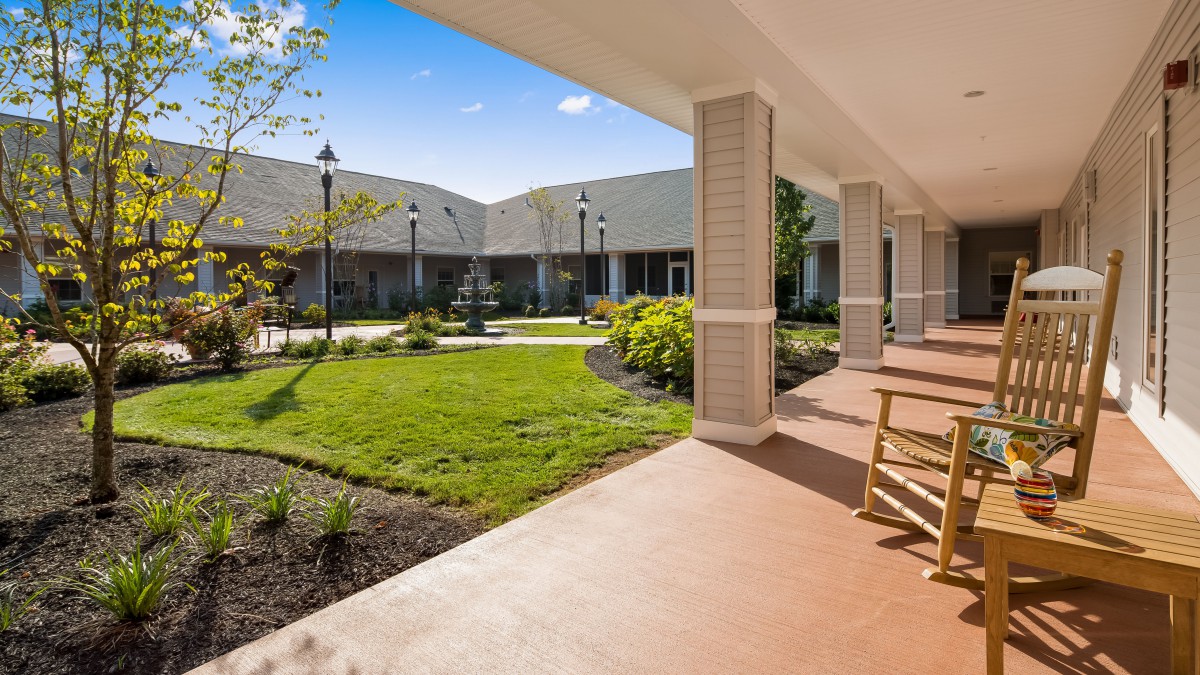 A peaceful courtyard with neatly maintained gardens and a covered veranda featuring rocking chairs.
