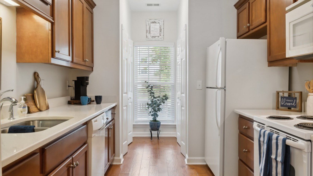 A bright kitchen with wooden cabinets, a white refrigerator, and an indoor plant near a sunlit window.