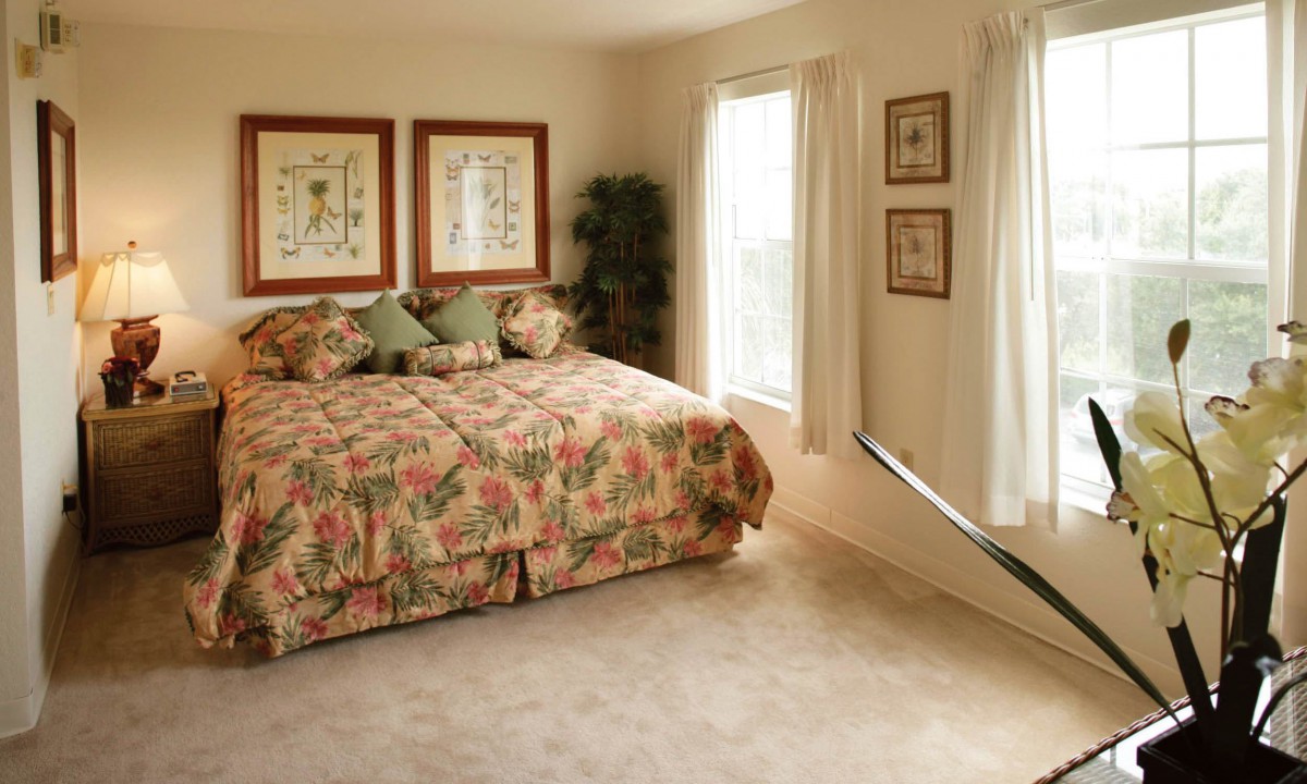A cozy bedroom with floral bedding and natural light streaming in through the windows.