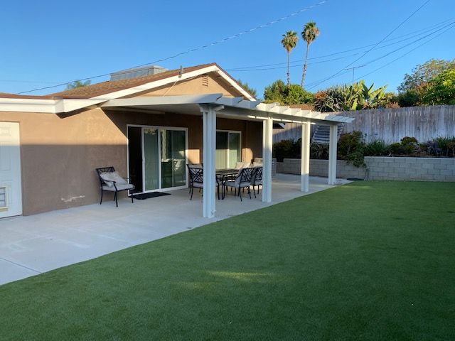 A modern house with a spacious backyard, featuring a patio and outdoor furniture under a clear blue sky.