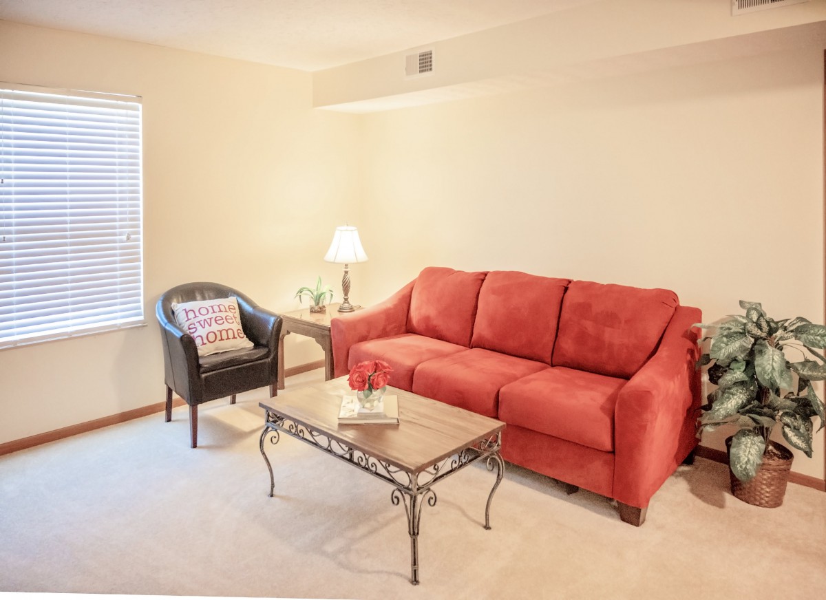 A cozy living room with a red sofa, armchair, and coffee table, illuminated by a lamp.