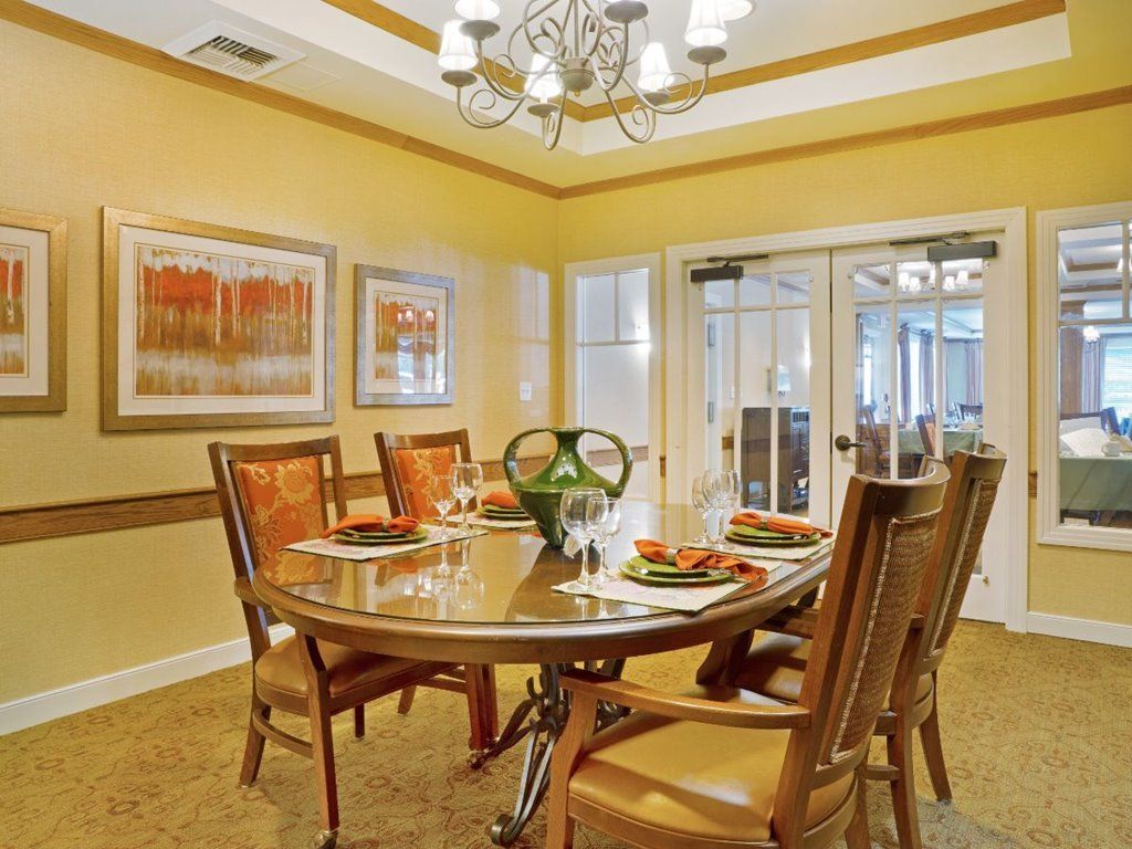 A warmly lit dining room with a round table set for four, featuring elegant decor and an overhead chandelier.