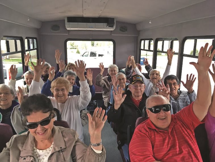 A group of elderly people happily raising their hands while traveling on a bus.