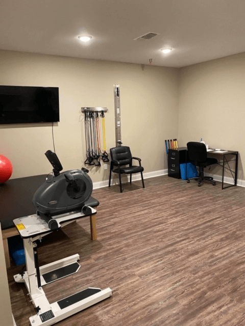 A well-equipped exercise room featuring a stationary bike, TV, and various workout tools for physical therapy.