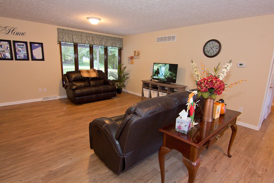 A cozy living room with leather sofas, a TV, and large windows providing natural light.