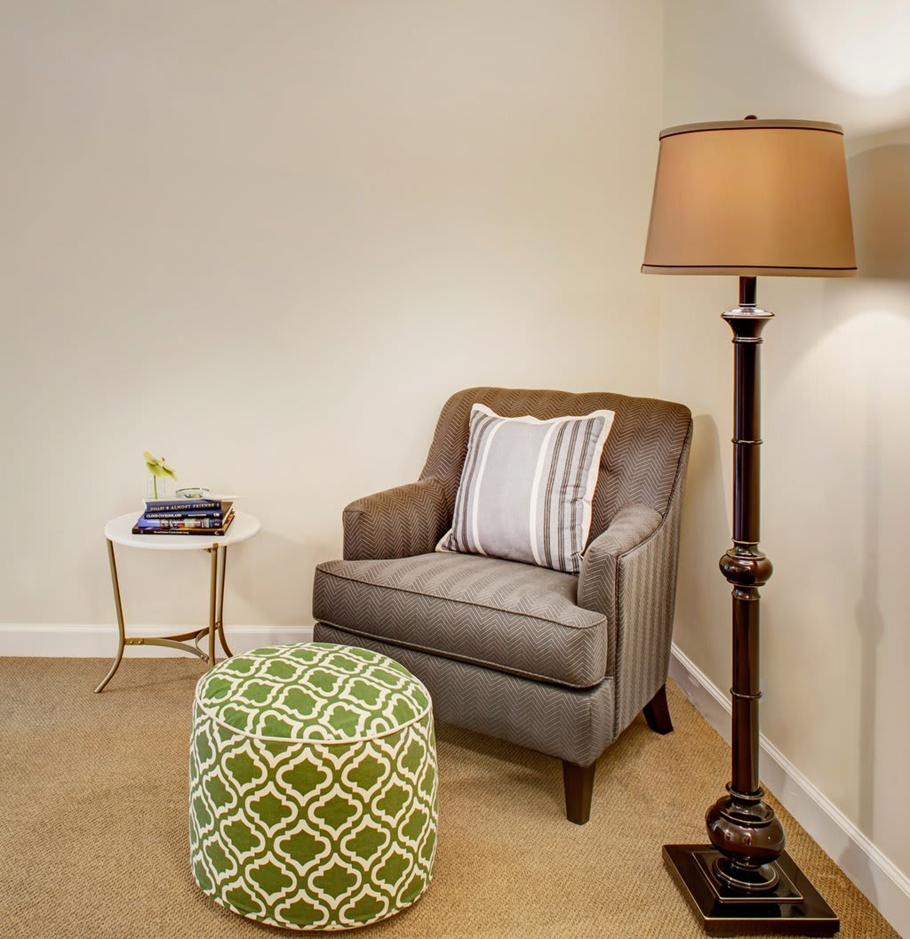 A cozy corner with a comfortable armchair, floor lamp, side table, and decorative pouf.