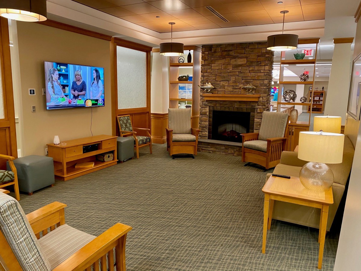 A cozy living room featuring a stone fireplace, television, and comfortable seating surrounded by bookshelves.