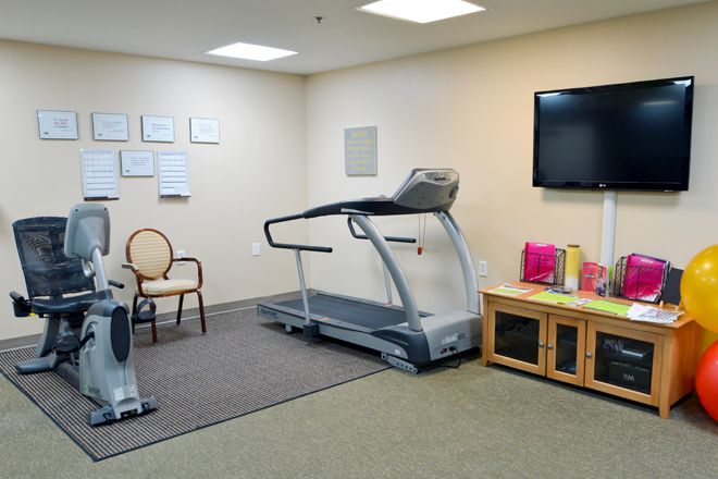 A small fitness room equipped with a treadmill, exercise bike, and a television.