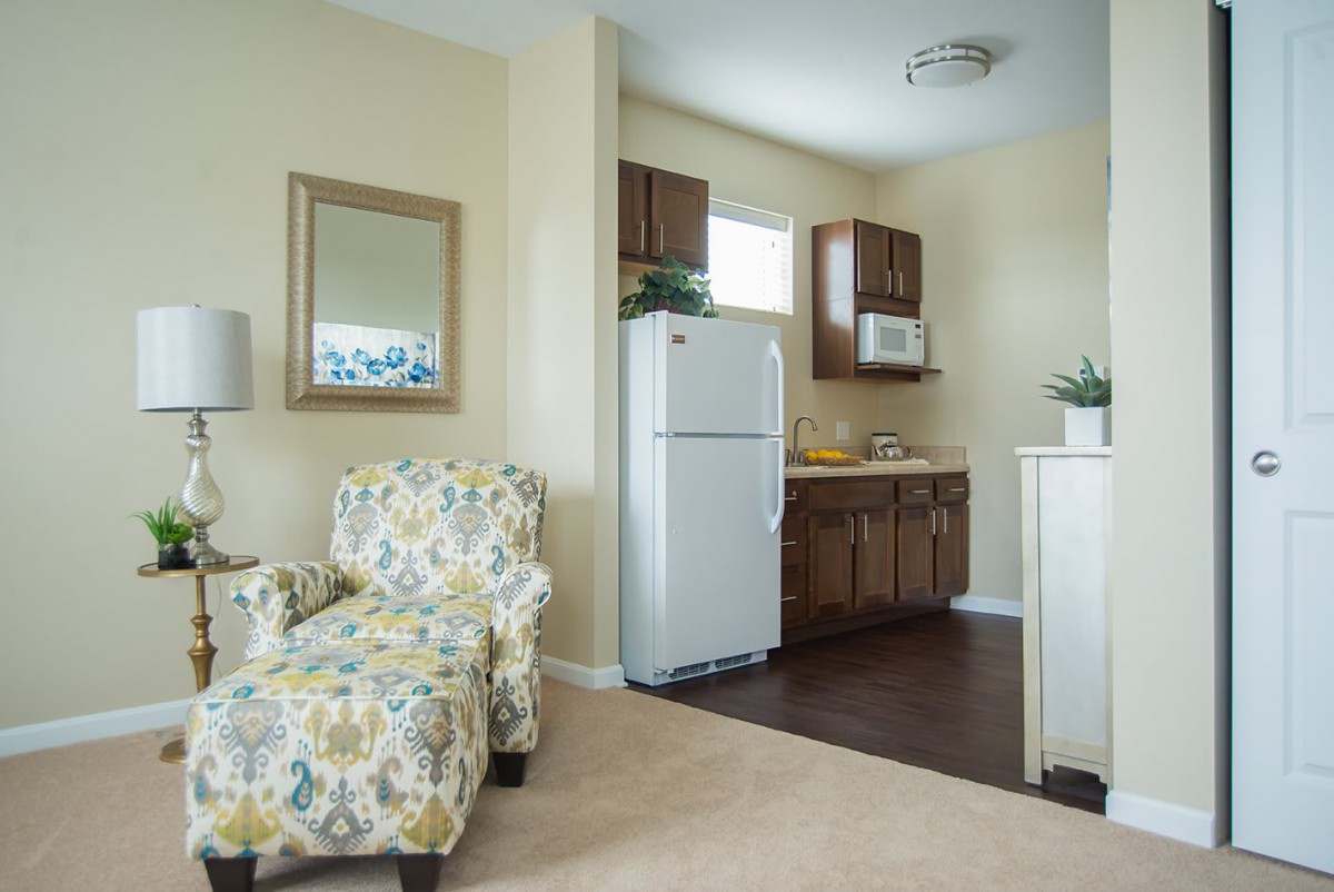 A cozy apartment interior featuring a small kitchenette and a floral armchair.