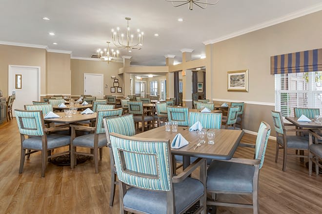A well-lit dining room with neatly arranged tables and chairs, featuring elegant light fixtures.
